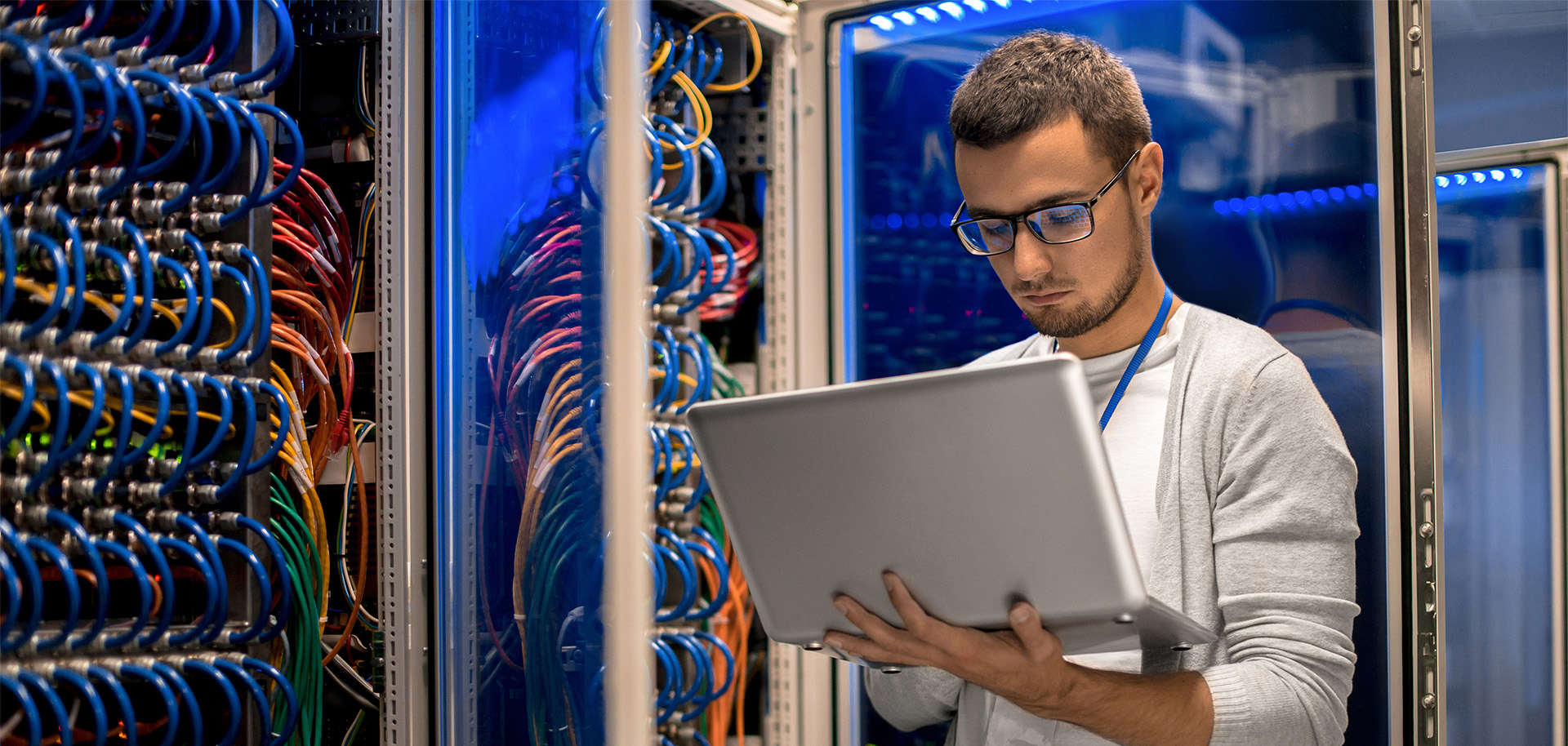 Man holding computer standing next to servers